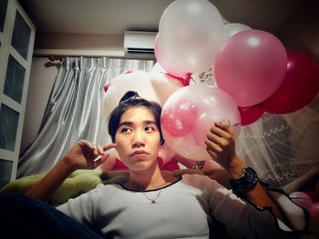 Young woman holding balloons while sitting on sofa at home