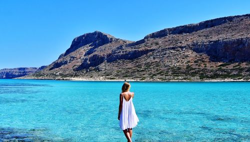 Rear view of woman standing by sea against clear blue sky