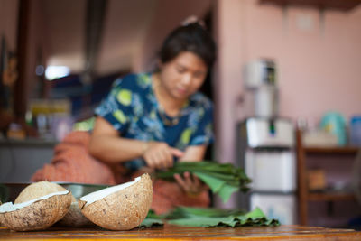 Close-up of coconut on cutting board with woman in background at home