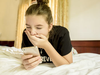 Low angle view of girl using mobile phone yawning while lying on bed at home