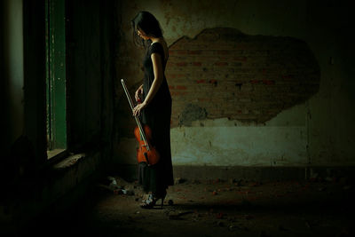 Side view of woman holding violin standing in old home