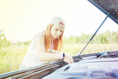 Woman checking engine of car by field