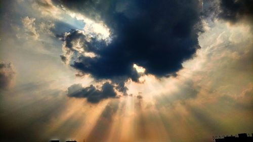 Low angle view of sunlight streaming through clouds