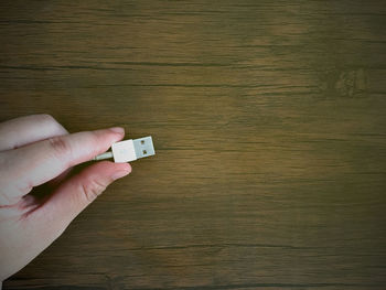 Close-up of hand holding wooden table against wall