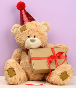 Cute brown teddy bear in a red cap sits and holds a brown box with a gift, festive background