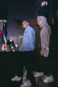 Side view of couple standing in illuminated city at night