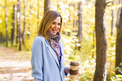 Portrait of smiling young woman standing against trees