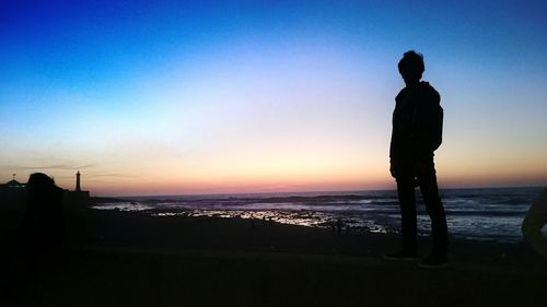 Silhouette man standing at beach against clear sky during sunset