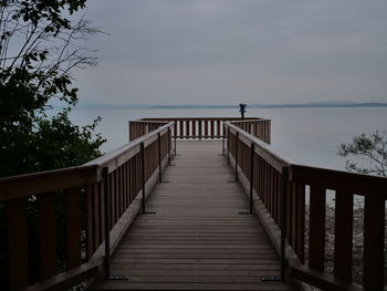 Wooden walkway by sea against sky