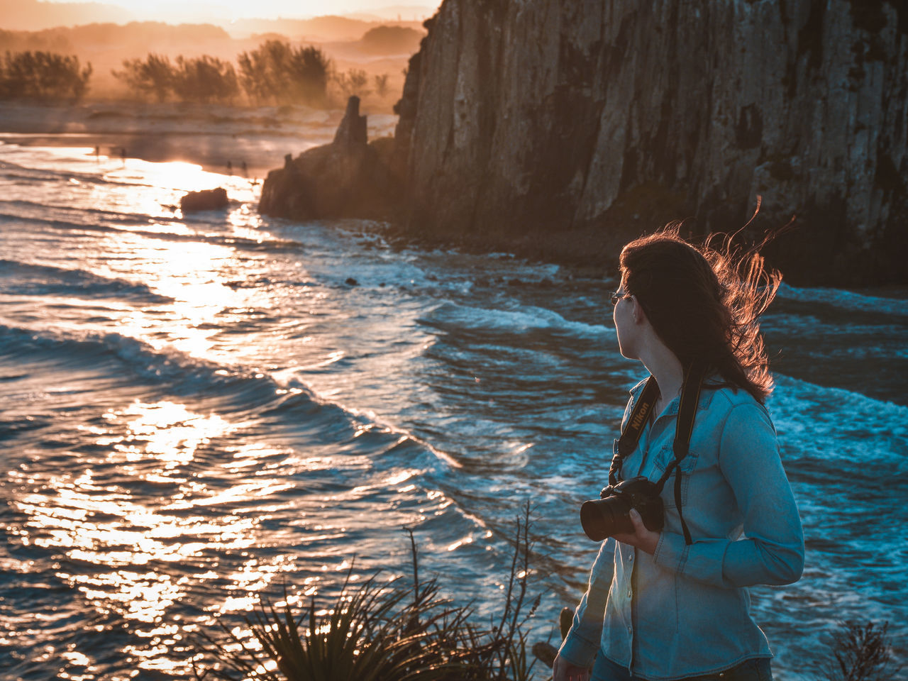 REAR VIEW OF WOMAN STANDING IN SEA AGAINST SUNSET SKY