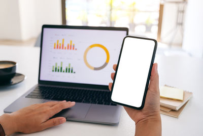 Midsection of man using smart phone and laptop on table