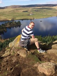 High angle portrait of man sitting on rock against lake