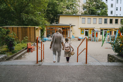 Rear view of senior woman with granddaughter walking towards kindergarten