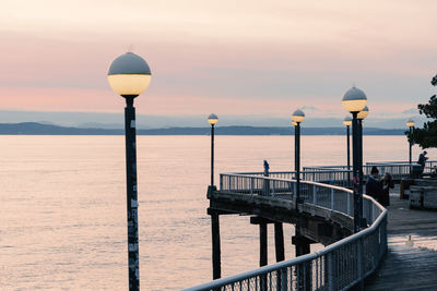 Illuminated street lights on pier by sea