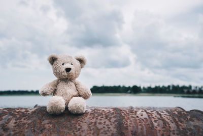 Stuffed toy on rusty metal by lake against cloudy sky