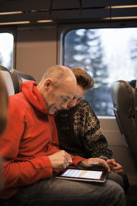 Man and teenage boy using tablet on train