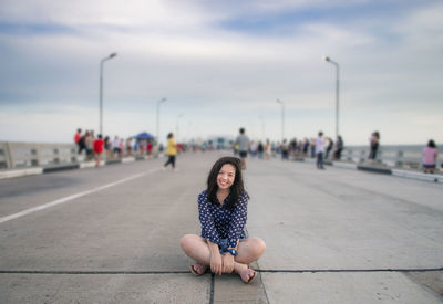 Portrait of woman sitting on street in city against sky