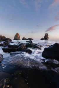 Rocks in sea against sky during sunset