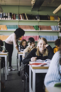 Smiling girl leaning on elbows while sitting at desk in classroom