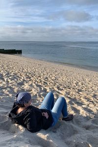 Man lying on sand at beach against sky