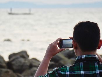 Rear view of man photographing sea through mobile phone