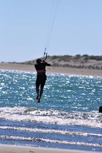Rear view of person kiteboarding at beach on sunny day