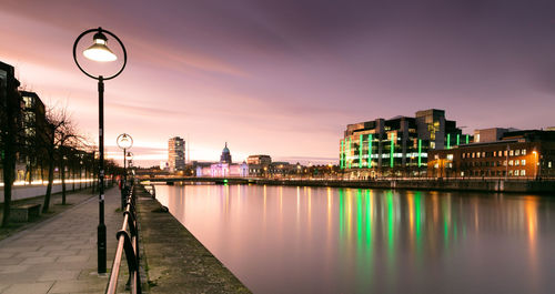 Illuminated street lights by river against sky at night