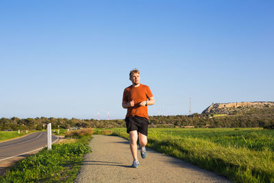 Full length of man running on road against clear blue sky