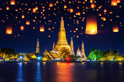 Illuminated paper lanterns flying over river in city at night