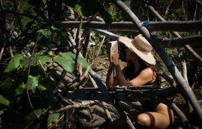 Midsection of young woman on tree in forest