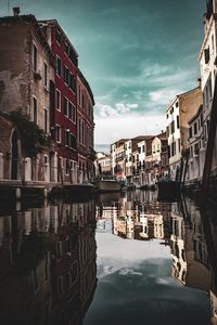 Canal amidst buildings in city against sky