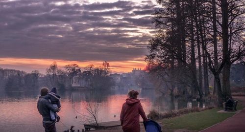 Rear view of people on shore against sky during sunset