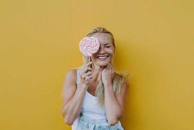 Smiling woman holding lollipop against yellow background