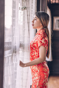 Side view of young woman standing by window