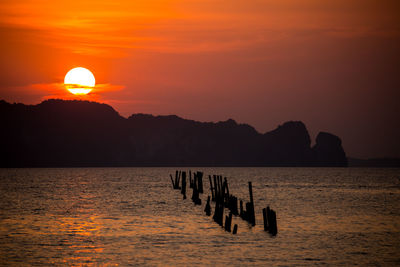 Silhouette wooden posts in sea against sky during sunset
