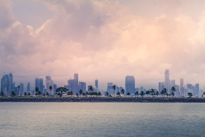 Sea by modern buildings against sky in city