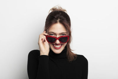 Smiling beautiful young woman wearing sunglasses against white background