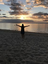 Woman with arms outstretched standing at beach during sunset