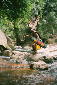 Mid adult man standing on rock wearing costume by river in forest