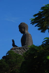 Low angle view of buddha statue against clear blue sky at lantau island