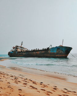 Abandoned ship in sea at beach against clear sky