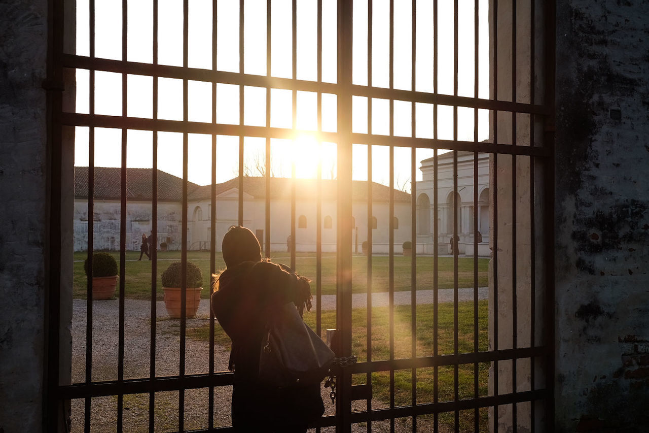 window, real people, architecture, sunlight, building, prison, one person, nature, built structure, rear view, punishment, outdoors, sun, lifestyles, men, day, sky, adult, lens flare