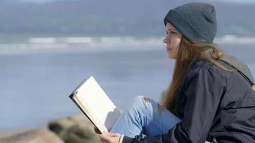 Side view of woman reading book against the sea