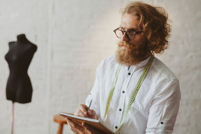 Fashion designer looking away while standing against brick wall in workshop