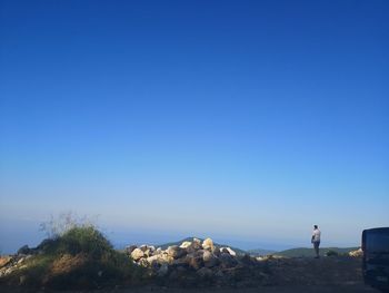 Man standing on rock against clear blue sky