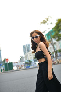 Young woman wearing sunglasses while standing against sky