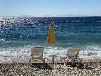 Empty chairs on beach against clear sky