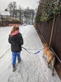 Rear view of girl with dog walking in snow