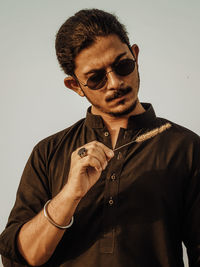 Young man wearing sunglasses while standing against wall