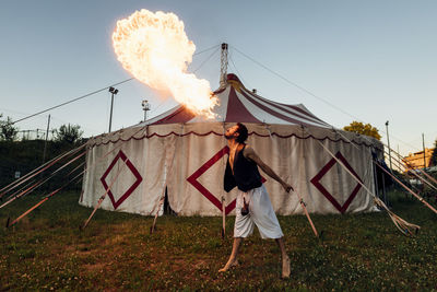 Male acrobat blowing fire while standing in front of circus tent